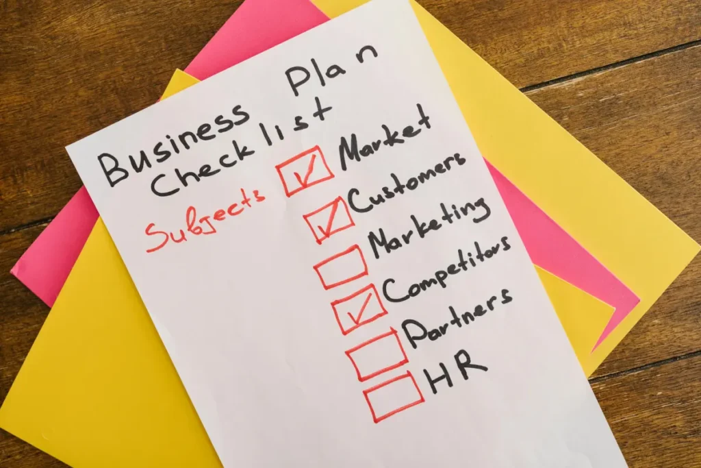 Catatan rencana bisnis yang ditulis tangan di atas meja dengan kertas-kertas warna-warni sebagai ilustrasi business plan